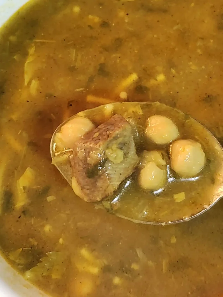 A bowl of Moroccan Harira soup served with noodles, chickpeas, and herbs.