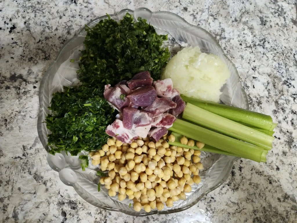 A plate of fresh Harira ingredients, including chopped parsley, cilantro, diced lamb meat, celery stalks, chickpeas, and grated onion, ready for cooking.