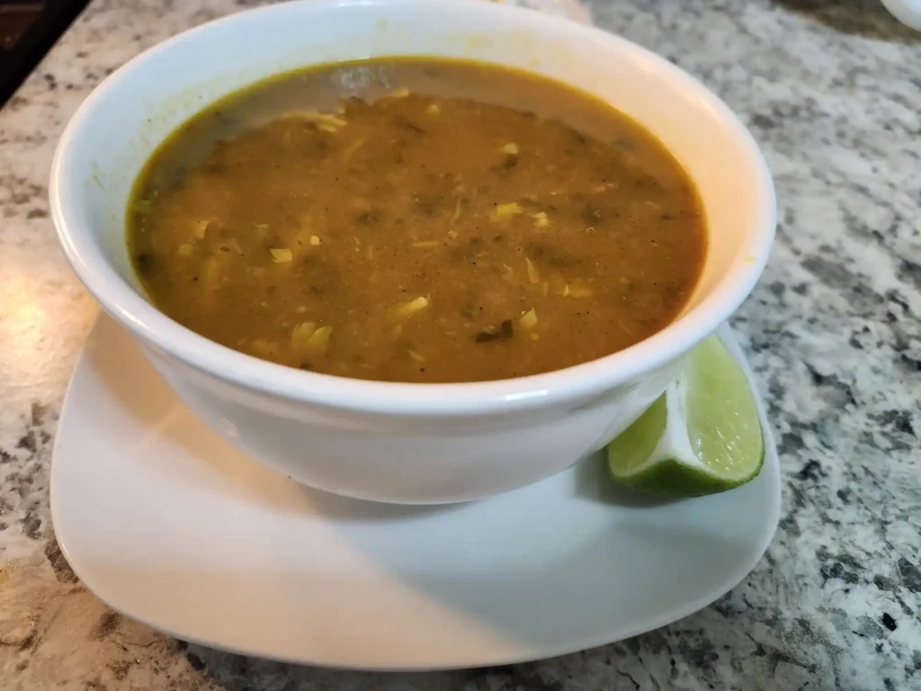 A bowl of Moroccan Harira soup served with noodles, chickpeas, and herbs, accompanied by  lime wedges.