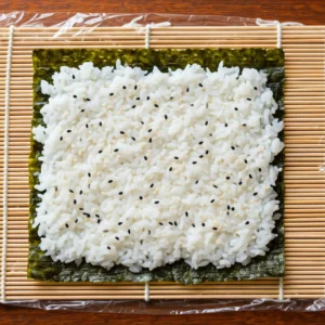 Next, scatter toasted white sesame seeds along with black sesame seeds over the rice. After that, turn the entire sheet of seaweed over.