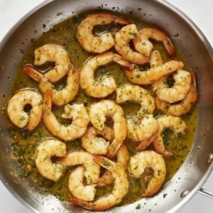 Shrimp cooking in a skillet with garlic butter sauce and herbs.