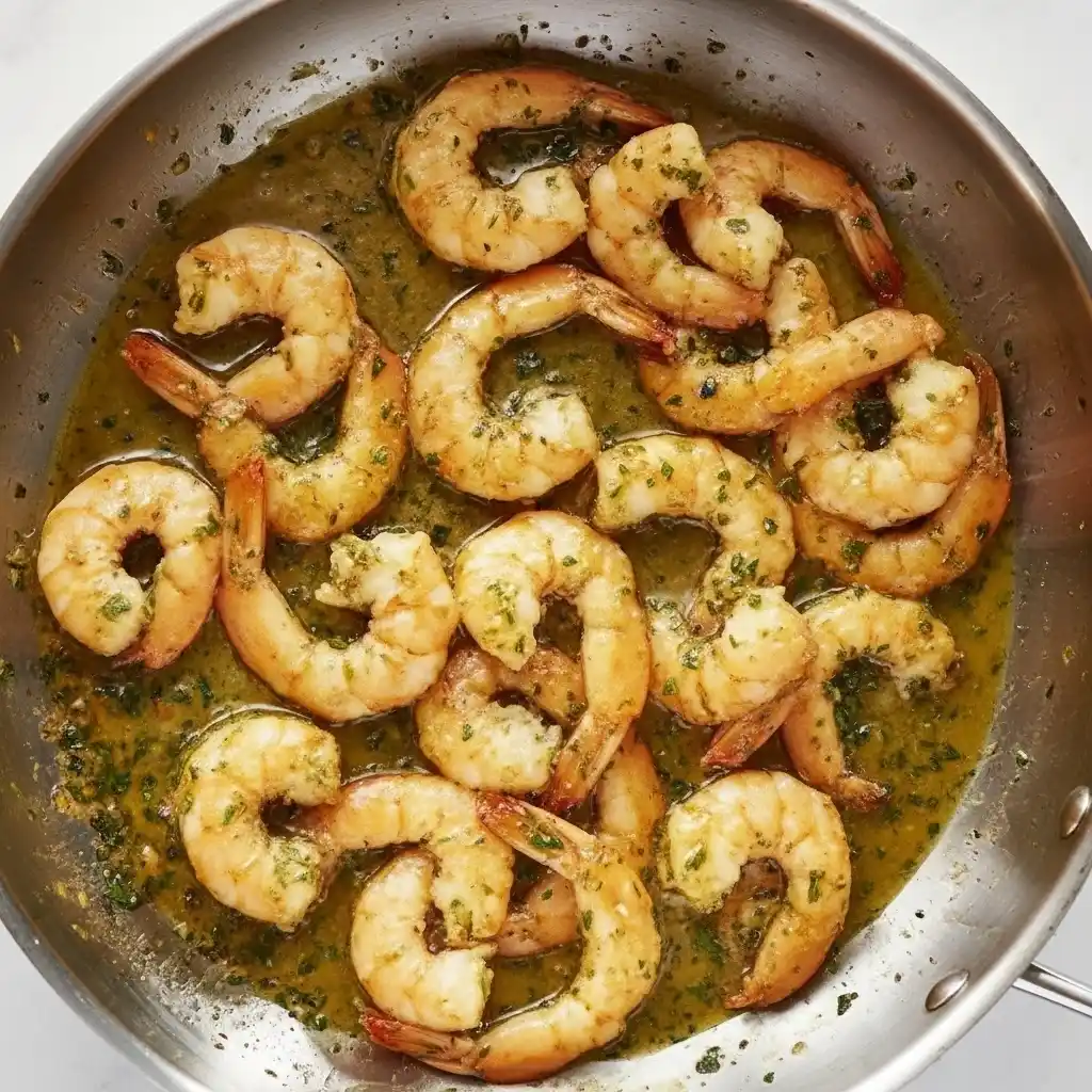 Shrimp cooking in a skillet with garlic butter sauce and herbs.