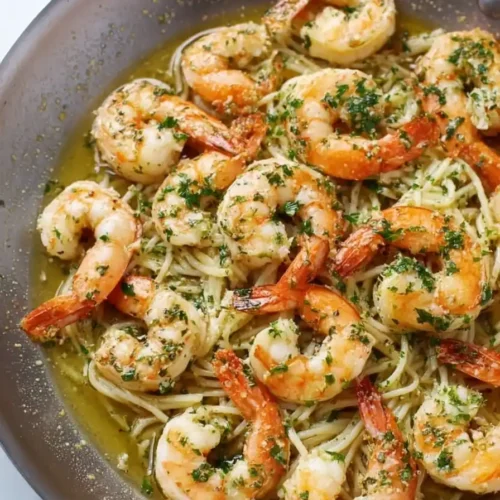 Shrimp scampi served over a bed of pasta in a skillet, topped with parsley.