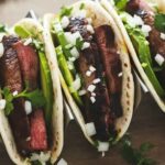 Three wagyu steak tacos on a wooden surface, filled with steak strips, avocado, onion, and cilantro.