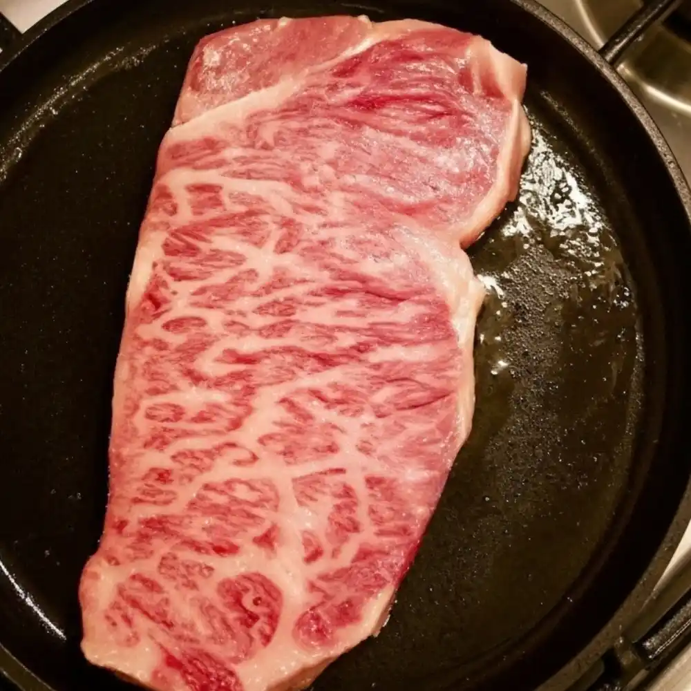 Raw Kobe beef steak with heavy marbling in a cast iron skillet, ready for searing.