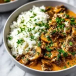 Bowl of creamy beef stroganoff with mushrooms and white rice, garnished with fresh parsley.