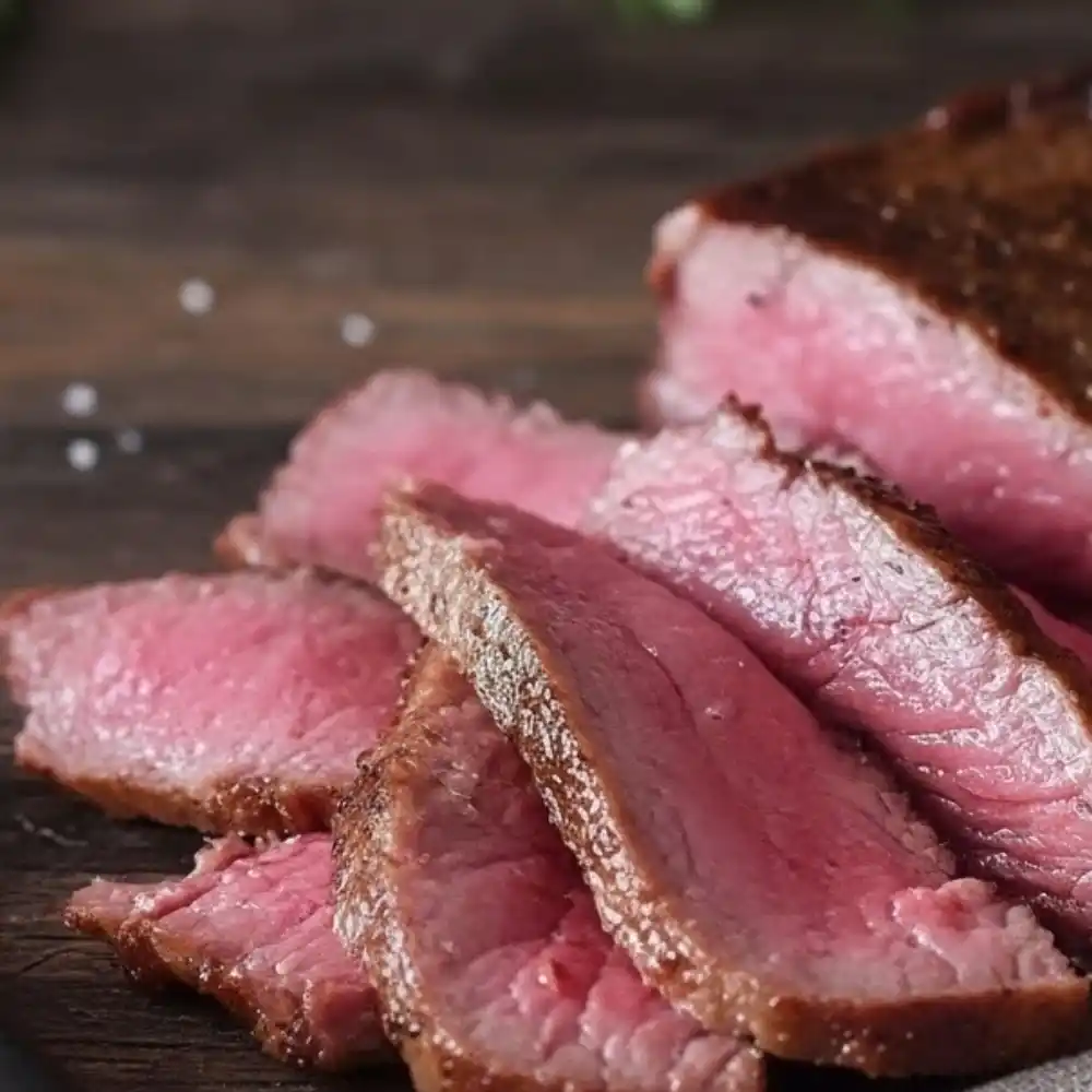 Slices of medium-rare wagyu steak on a wooden cutting board, showing a pink interior with a seared brown crust.