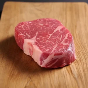 Raw wagyu ribeye steak on a wooden board, showcasing marbling of fat through the red meat.