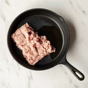 Uncooked ground chicken in a black skillet with olive oil before browning for tacos