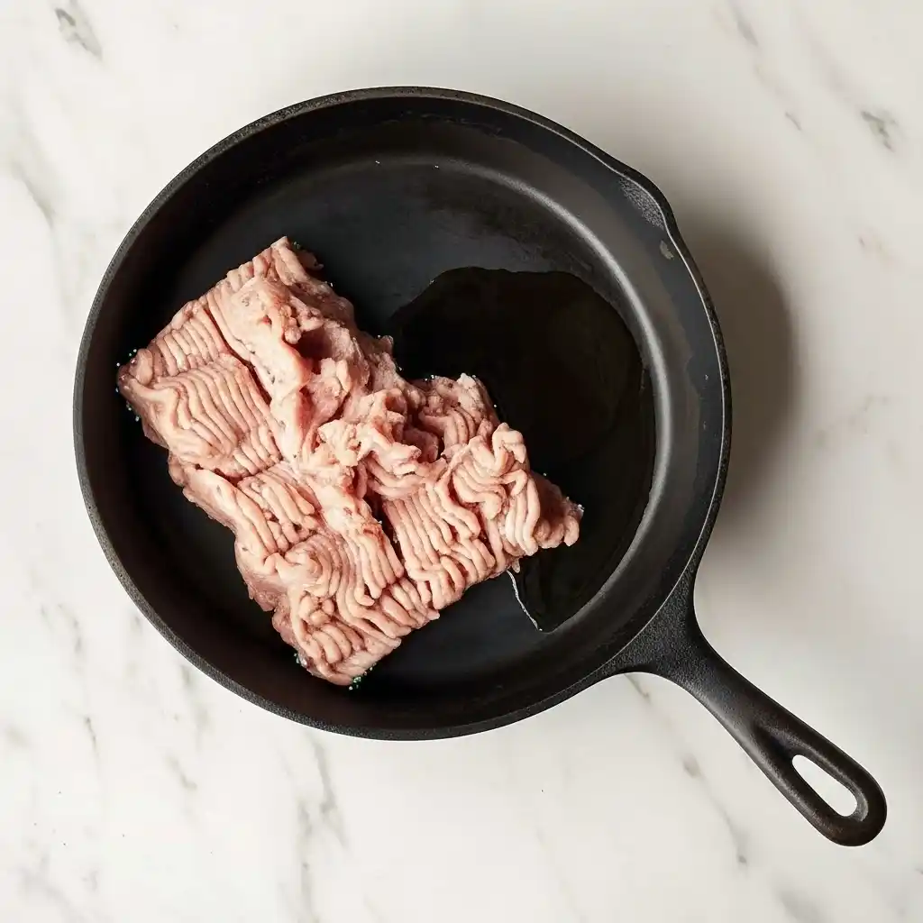 Uncooked ground chicken in a black skillet with olive oil before browning for tacos