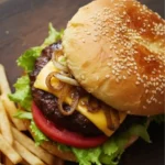 Kobe beef cheeseburger with lettuce, tomato, caramelized onions, and melted cheddar on a brioche-style sesame bun, served with fries.