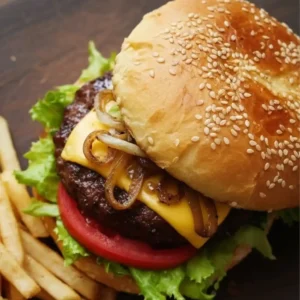 Kobe beef cheeseburger with lettuce, tomato, caramelized onions, and melted cheddar on a brioche-style sesame bun, served with fries.