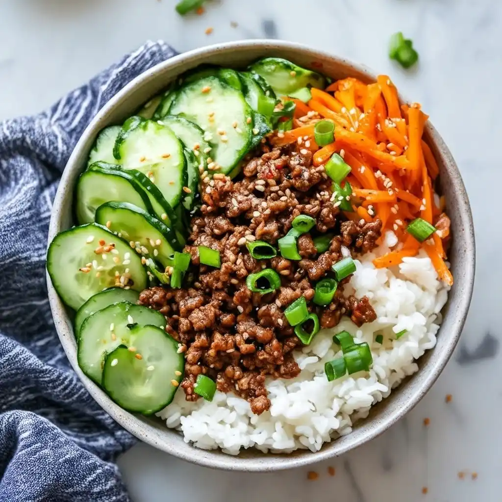 Healthy Korean beef bowl recipe with rice, cucumbers, carrots, ground beef, and sesame seeds