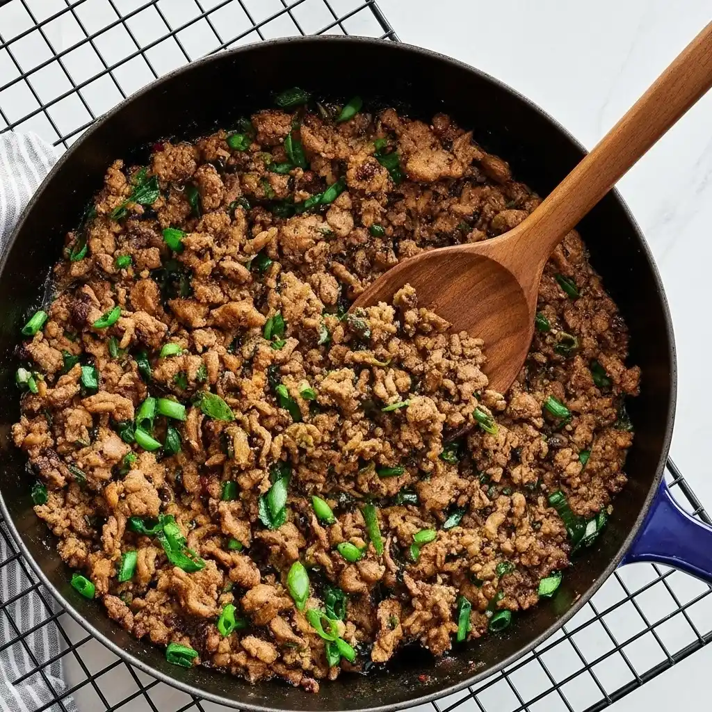 Ground beef cooking in skillet with green onions for Korean beef bowl recipe, savory step preparation