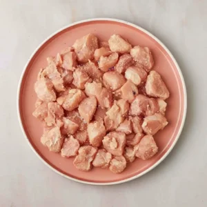 Raw chicken breast pieces on a pink plate seasoned with salt and pepper