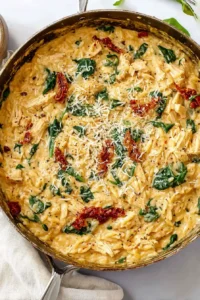 Creamy Marry Me Chicken Orzo with sun-dried tomatoes, spinach, and parmesan in a skillet