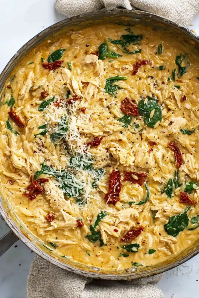 Overhead view of Marry Me Chicken Orzo with spinach, sun-dried tomatoes, and parmesan in a skillet