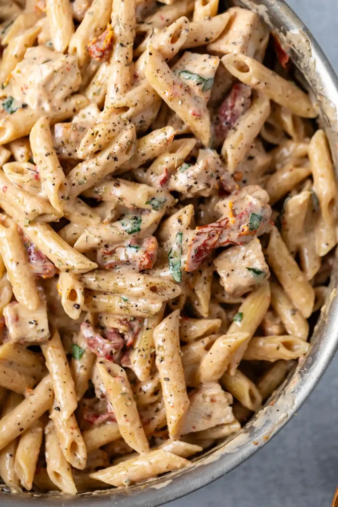 Penne pasta tossed in creamy garlic parmesan sauce with juicy chicken and sun-dried tomatoes, topped with herbs.