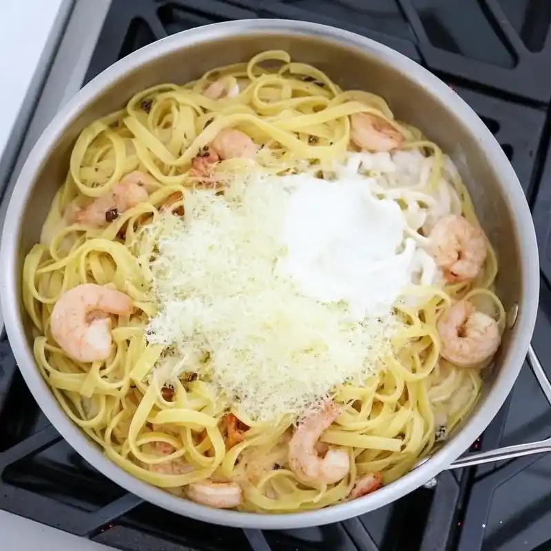 Pasta, shrimp, cream, and Parmesan mixing together in a skillet