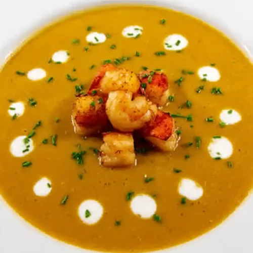 A bowl of lobster and shrimp bisque garnished with fresh herbs. Creamy, dairy-free seafood soup made with coconut milk, perfect for dinner.