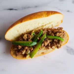 Assembling ground beef Philly sandwich with peppers on toasted roll