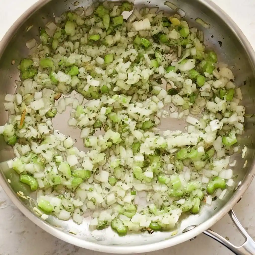 Onion, celery, and herbs sautéing in butter in a pan for shrimp bisque recipe