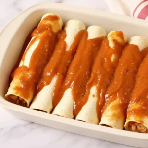 pouring enchilada sauce over rolled tortillas