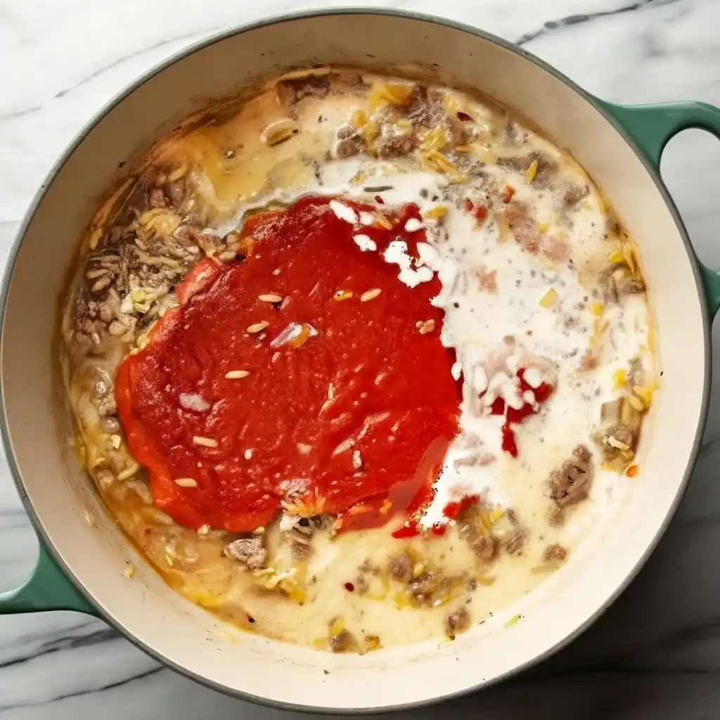 Adding tomato sauce and cream to ground beef orzo mixture