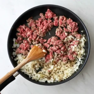stirring ground beef and onion mixture with wooden spoon