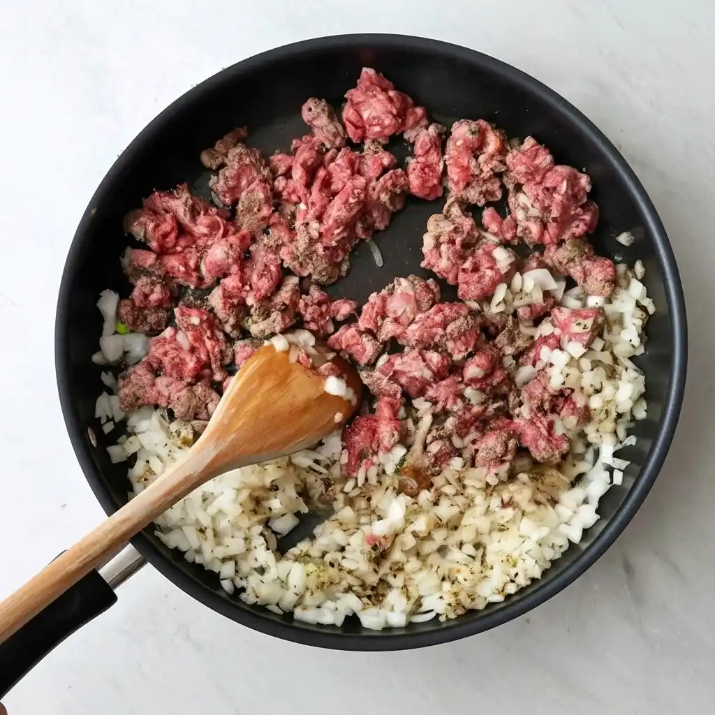 stirring ground beef and onion mixture with wooden spoon
