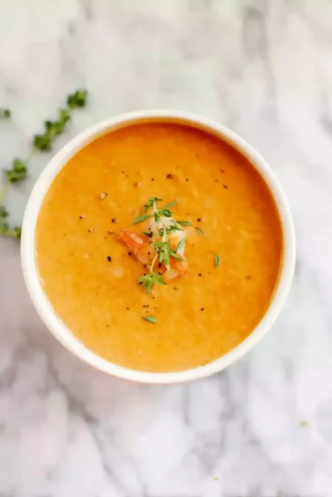 Creamy shrimp bisque topped with herbs on marble background