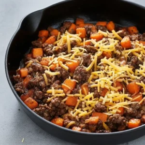 Diced sweet potatoes and tomatoes added to cooked beef in skillet with seasoning.