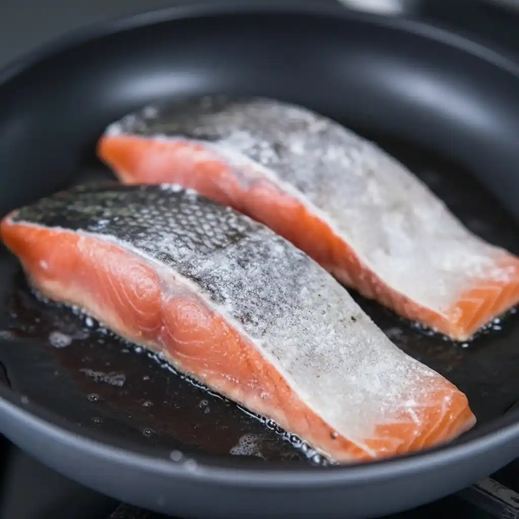 salmon fillets cooking skin side down in skillet
