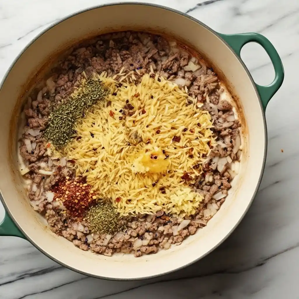 Stirring orzo and Italian herbs into ground beef tomato sauce
