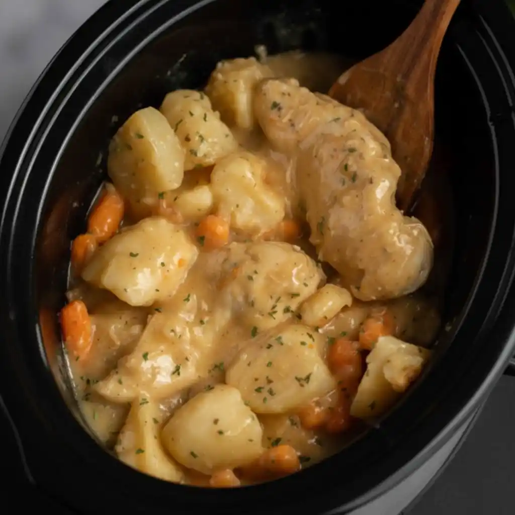 Creamy ranch chicken cooking in crock pot with potatoes and carrots.