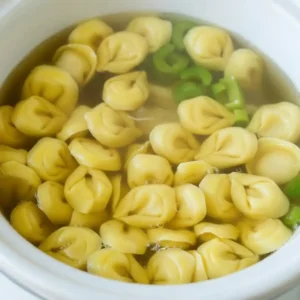 Cheese tortellini simmering in chicken broth inside a slow cooker