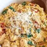 Orzo chicken with spinach and sun-dried tomatoes in white bowl