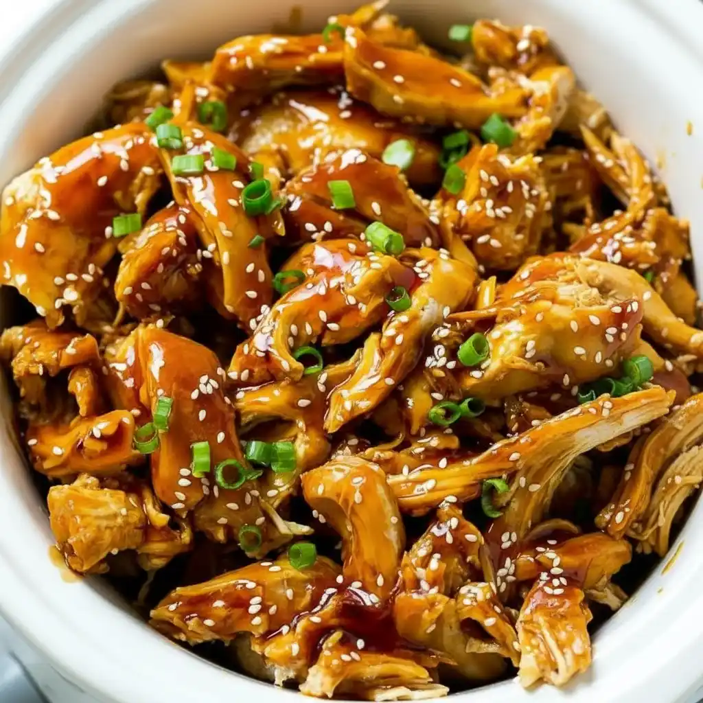 Dump and Go Teriyaki Chicken in crockpot being mixed with tongs and garnished with green onions