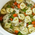 Ladle lifting chicken tortellini soup with carrots, celery, and parsley