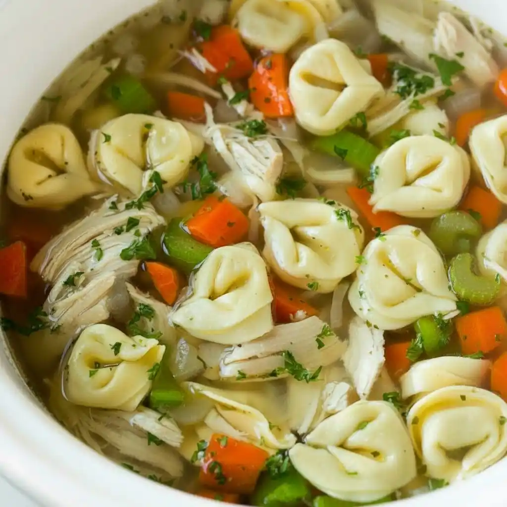 Ladle lifting chicken tortellini soup with carrots, celery, and parsley