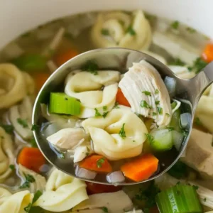 Overhead view of crockpot chicken tortellini soup with vegetables and herbs