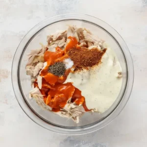 Bowl filled with shredded chicken, buffalo sauce, ranch dressing, and Cajun seasoning ready to make Buffalo Chicken Sliders.